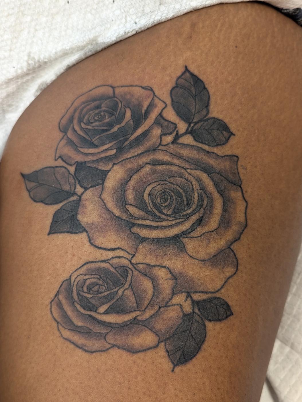 Three roses tattooed in black and gray ink on a shoulder.